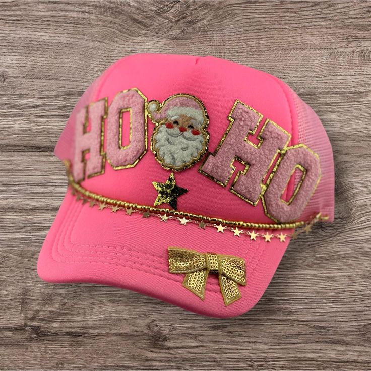 a pink hat with gold lettering and a santa clause on the front, sitting on top of a wooden surface