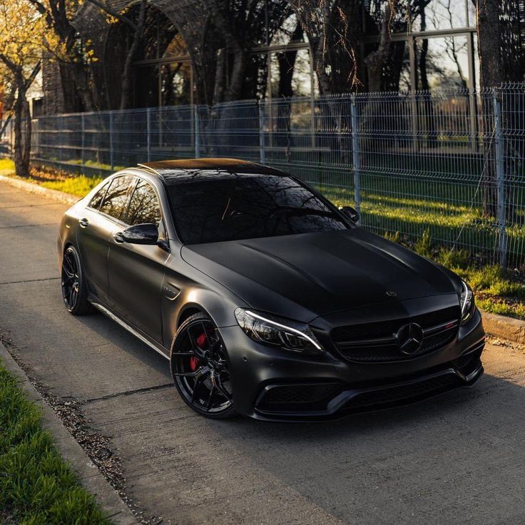 a black mercedes cla is parked on the side of the road in front of a fence