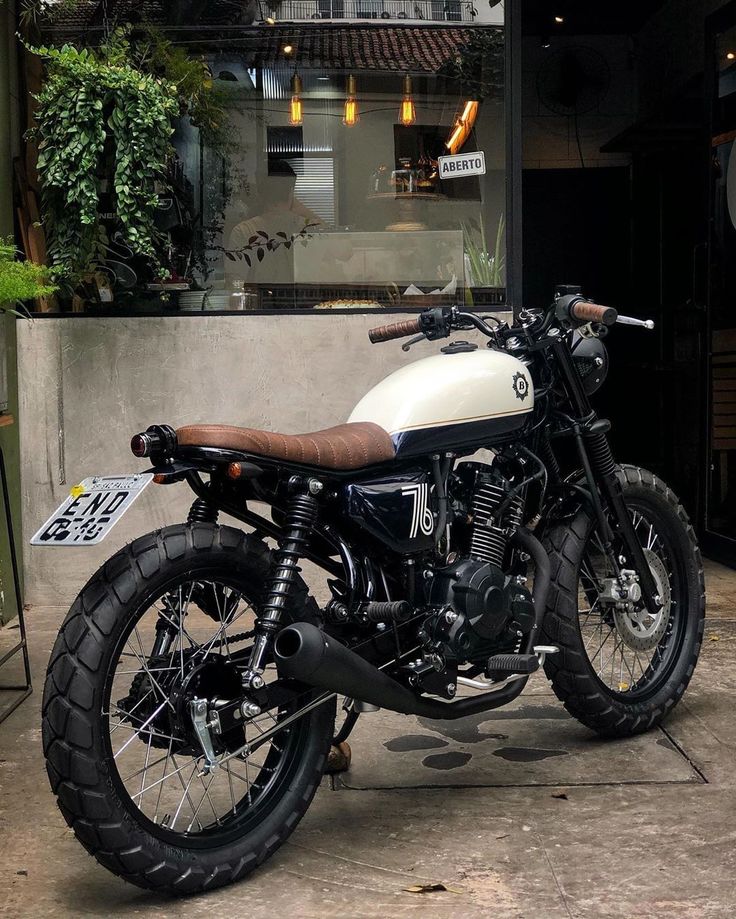 a white and black motorcycle parked in front of a building next to a planter