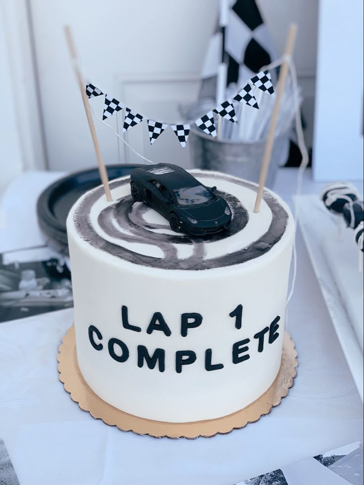 a birthday cake with a race car on top and lap 1 complete flags in the middle