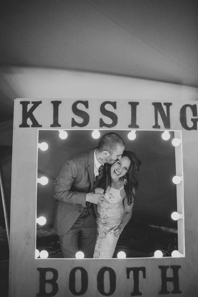 a black and white photo of a couple kissing in front of a lighted booth sign