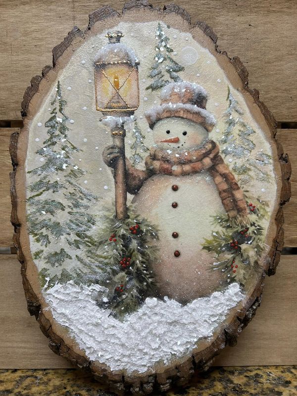 a snowman holding a lantern on top of a tree stump