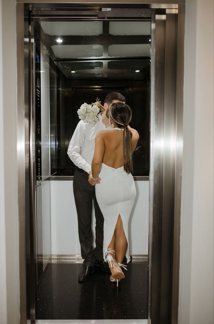 a man and woman are standing in an elevator, one is wearing a white dress