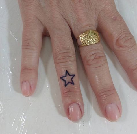 a woman's hand with a ring and star tattoo on her left index finger