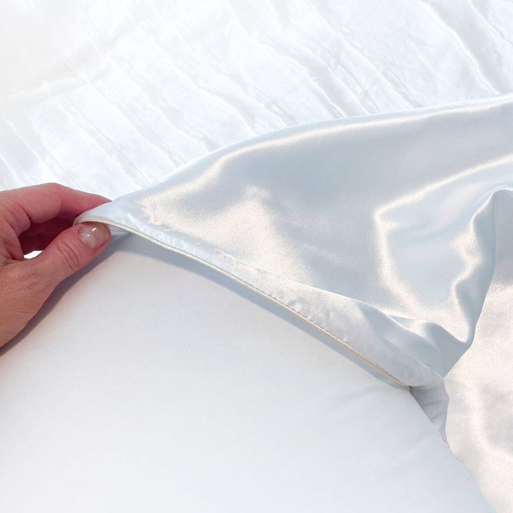 a person's hand is pulling up the side of a white sheet that has been folded over