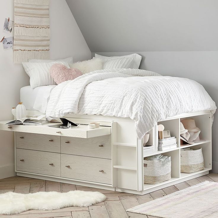 a white bed sitting under a slanted ceiling next to a dresser and shelf filled with books