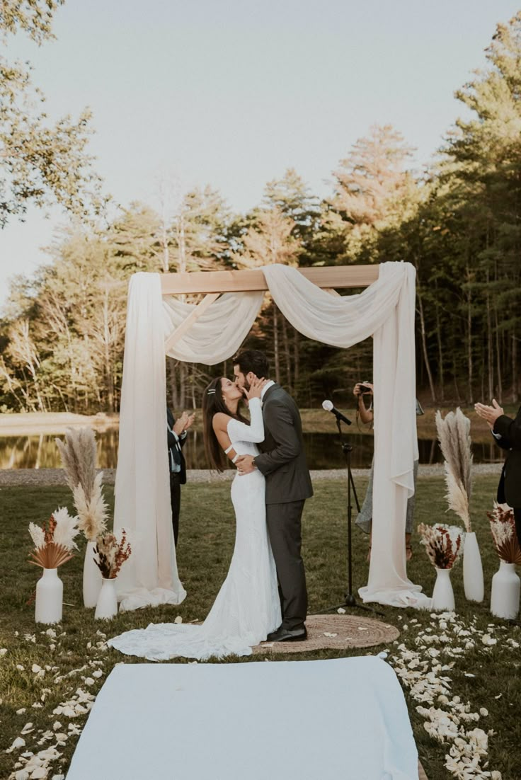 a bride and groom kissing under an outdoor wedding ceremony arch with flowers on the ground