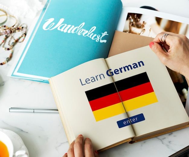 a person holding an open book on top of a table next to other books and glasses