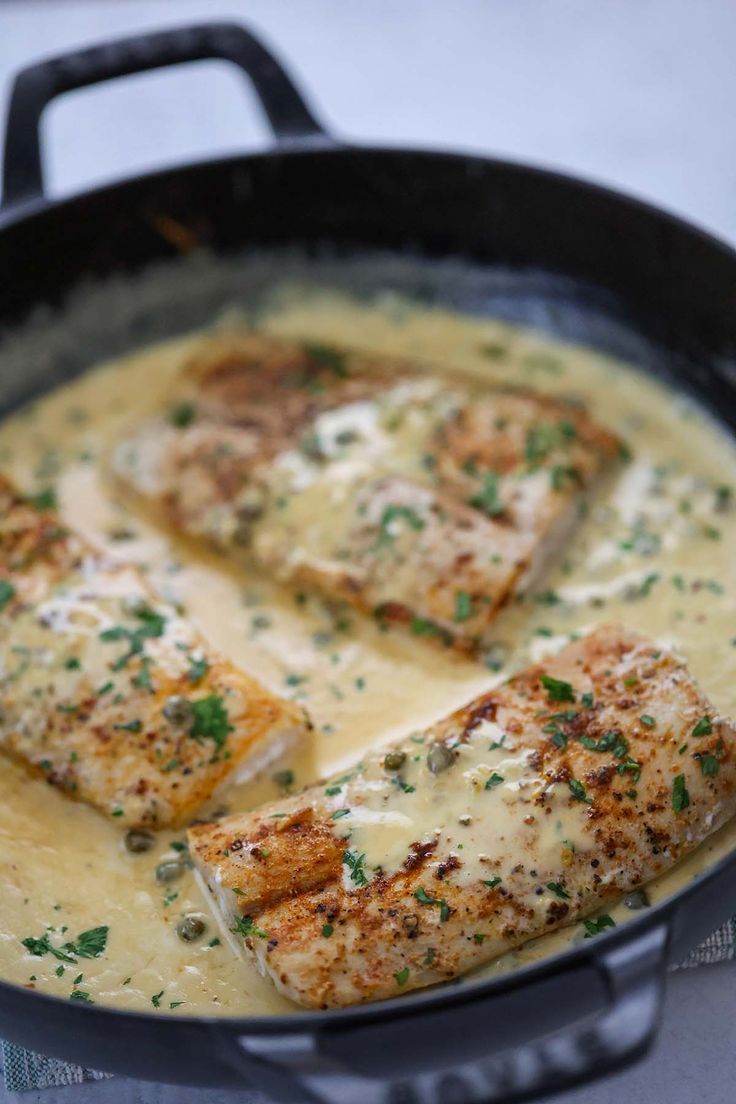 some fish is cooking in a skillet with cheese sauce on the side and parsley sprinkled on top