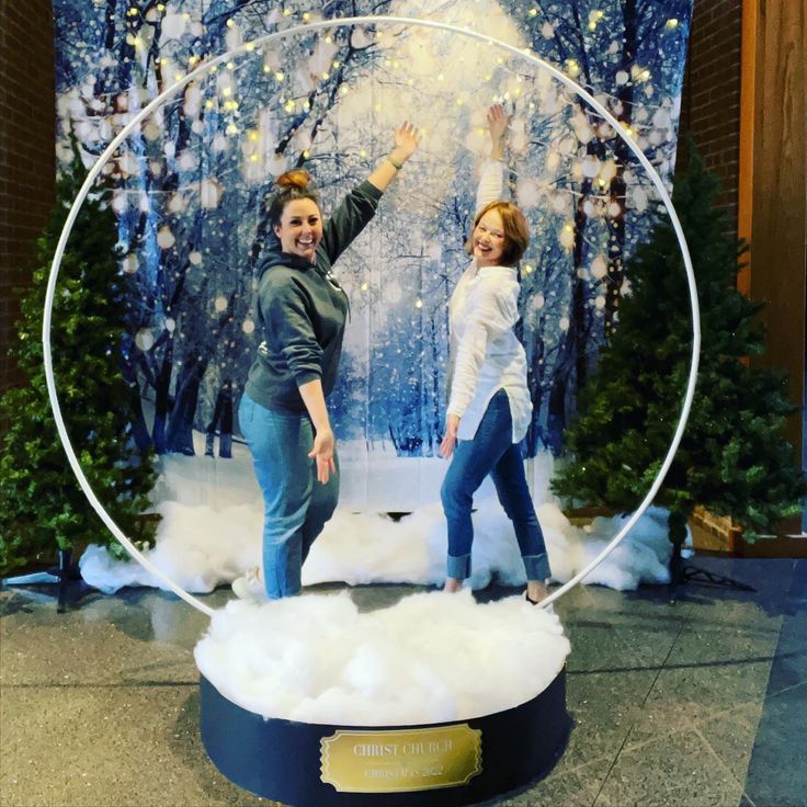 two women standing in front of a fake snow globe