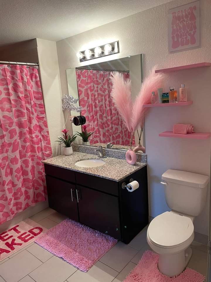 a bathroom with pink and white decor on the shower curtain, rugs and toilet