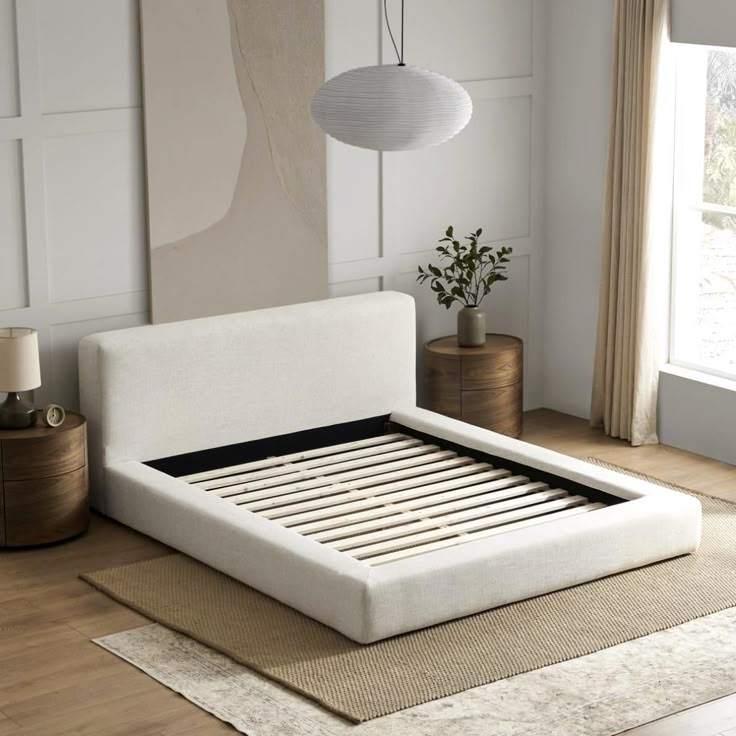 a white bed sitting on top of a wooden floor next to a lamp and window