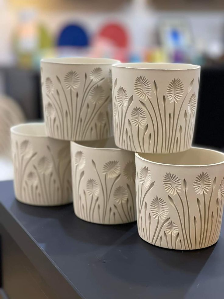 four white flower pots sitting on top of a black table next to each other in front of a blurry background