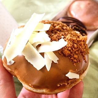 a hand holding a chocolate covered doughnut with toppings