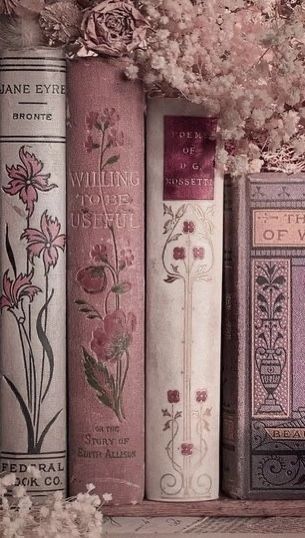 several books are lined up on a shelf with flowers in the middle and one is pink