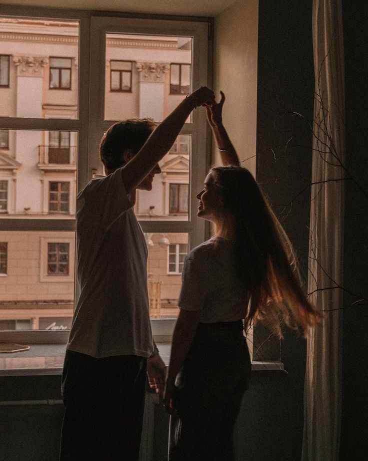 a man and woman standing next to each other in front of a window holding hands