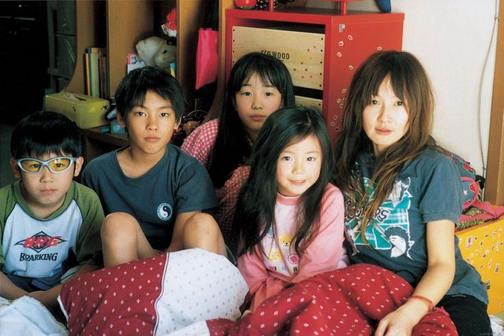 a group of young people sitting next to each other on top of a bed in a bedroom