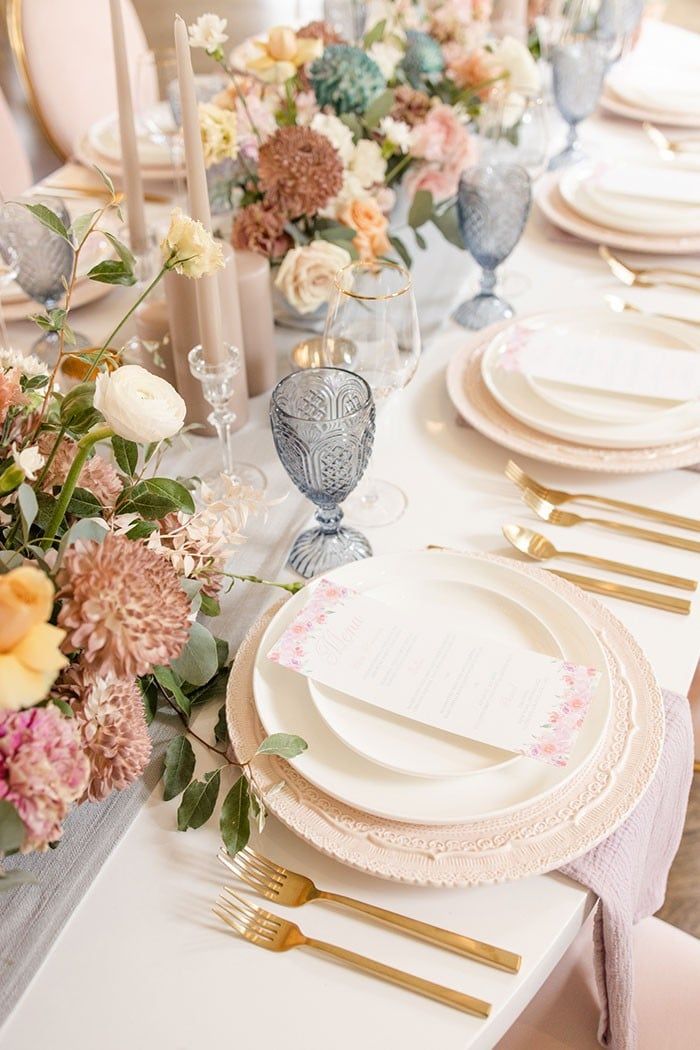 the table is set with white plates and gold place settings, pink floral centerpieces