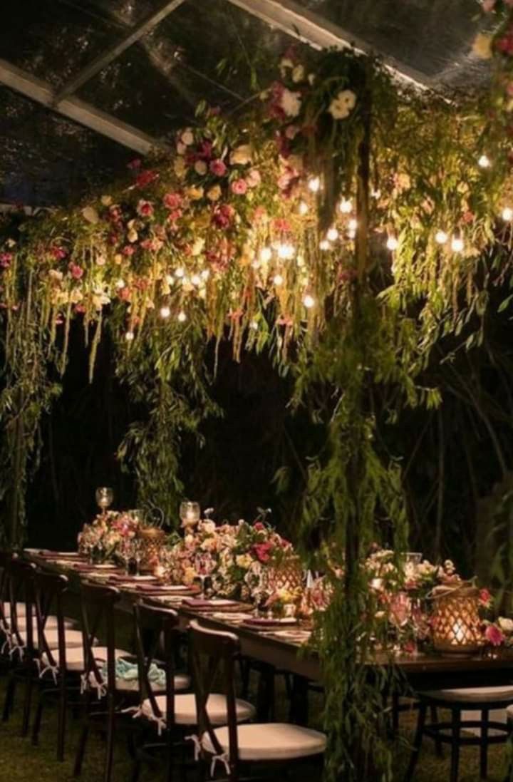 a long table with flowers and greenery hanging from the ceiling