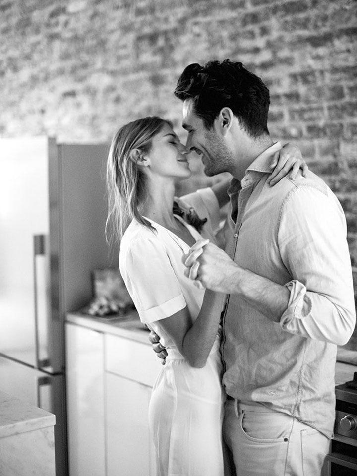 a man and woman standing next to each other in front of a brick wall kissing