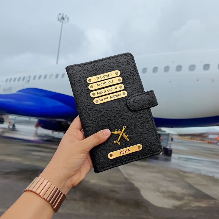 a person holding up a black book with gold writing on it and an airplane in the background