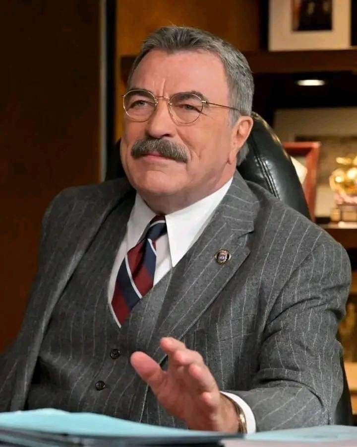 a man in a suit and tie sitting at a desk with his hands out to the side