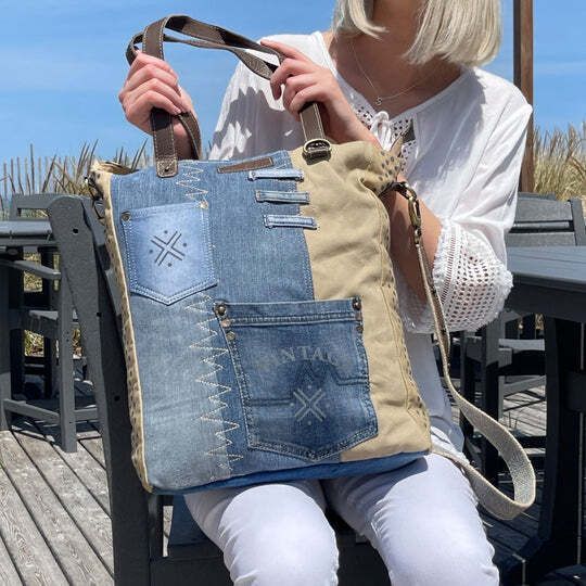 a woman is sitting on a bench holding a denim tote bag with holes in it