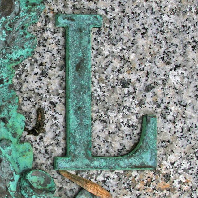 the letter j is made out of rusty green metal on a granite surface with a pencil