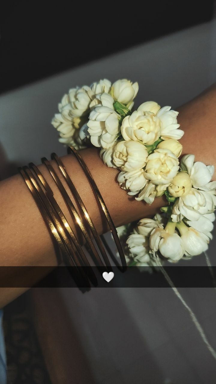 a woman's arm with bracelets and flowers on it, the wrist is holding a bouquet of white roses