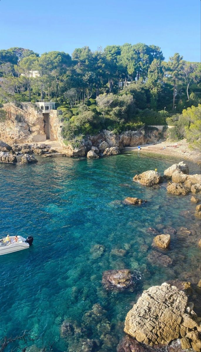 a boat is in the clear blue water near some rocks and trees on the shore