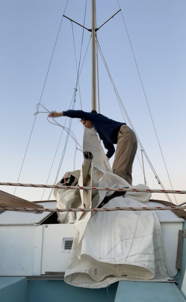 a man on top of a sailboat working on something white and blue in the water