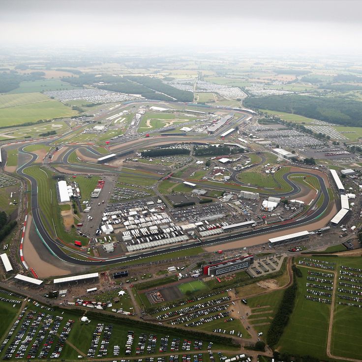 an aerial view of a race track with cars parked in the lot and buildings around it