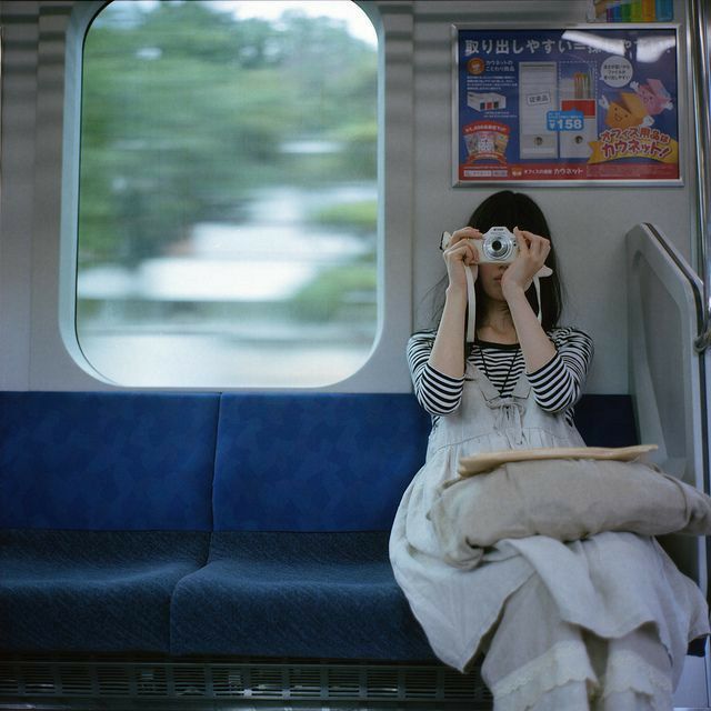 a woman sitting on a train holding a camera up to her face while looking out the window