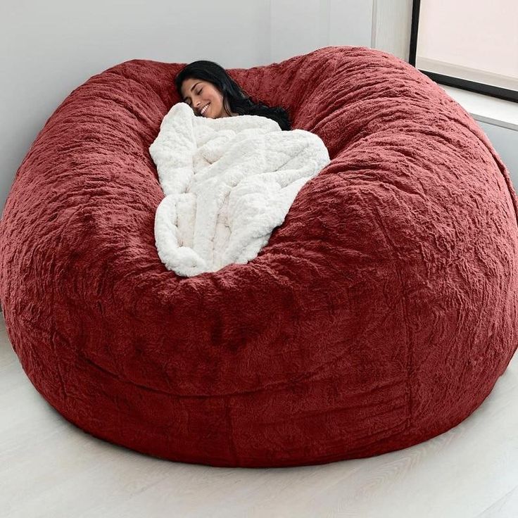 a woman wrapped in a blanket is sitting on a large red bean bag chair with white fur