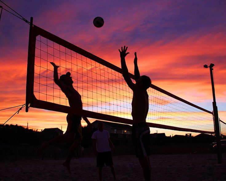 three people playing volleyball on the beach at sunset