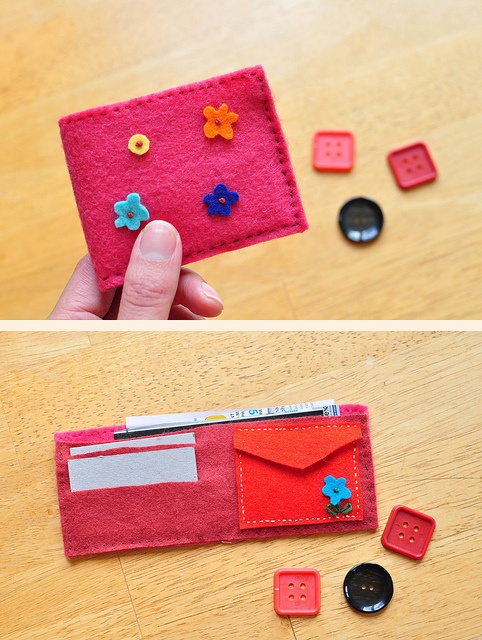 a hand holding a red felt wallet with buttons and magnets attached to it on top of a wooden table