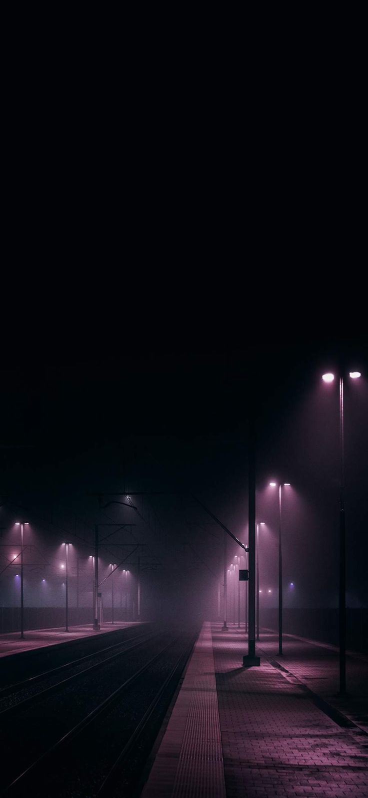 an empty train station at night with lights on and fog in the air over the tracks