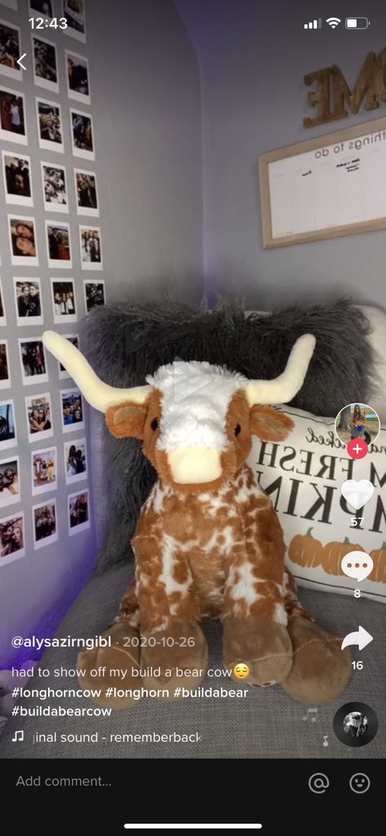 a stuffed cow sitting on top of a bed next to a wall with pictures behind it