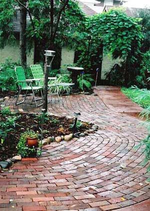 a brick patio surrounded by greenery and chairs