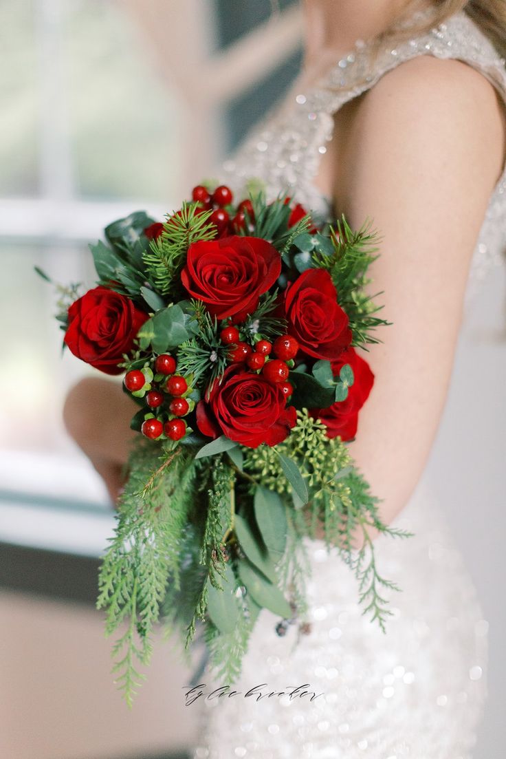 a bride holding a bouquet of red roses and greenery