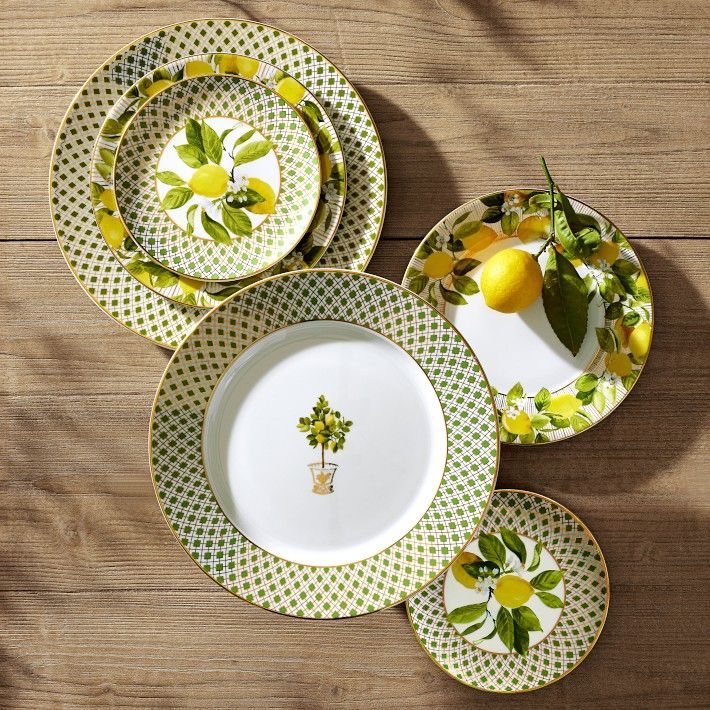 four plates with lemons and leaves on them sitting on a wooden table next to each other