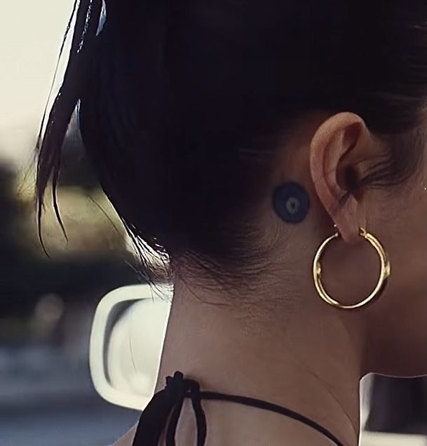 a woman wearing large gold hoop earrings on her neck and behind her ear, looking off into the distance