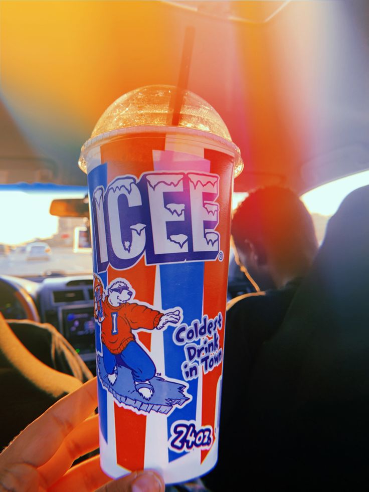 a person holding up a drink in the back seat of a car with an ice cream advertisement on it