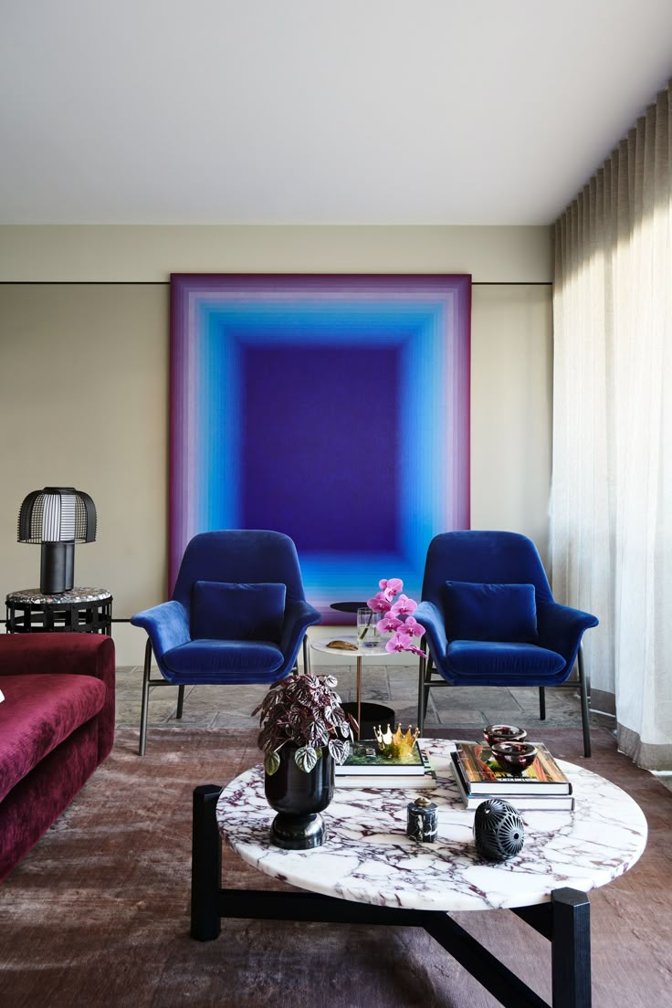 a living room with two blue chairs and a coffee table in front of a painting