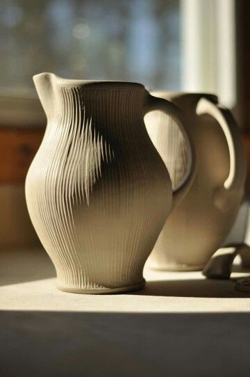 two white vases sitting next to each other on a window sill in the sunlight