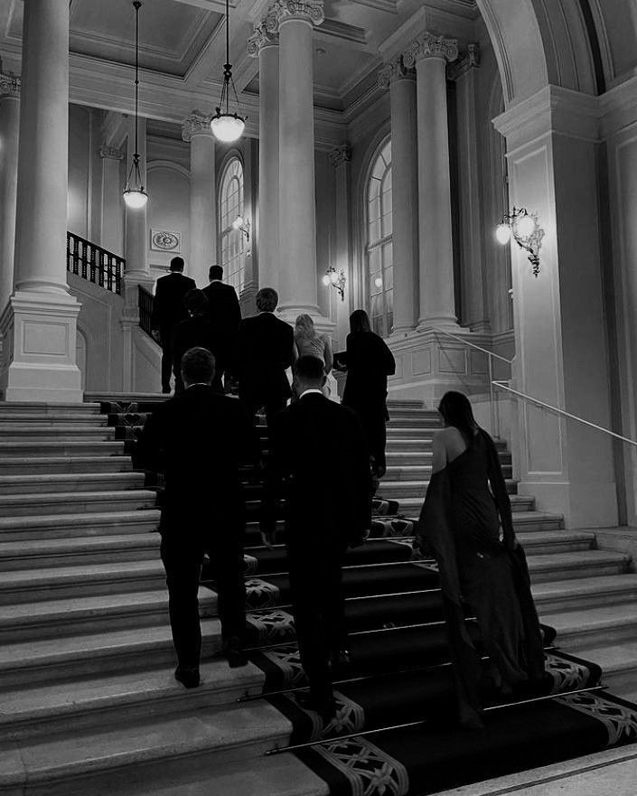 black and white photograph of people walking up the stairs in an old building with columns