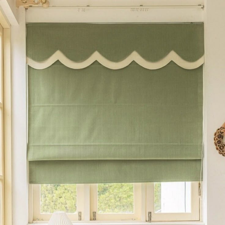 a green roman blind with white scallops on the top and bottom, in front of a window