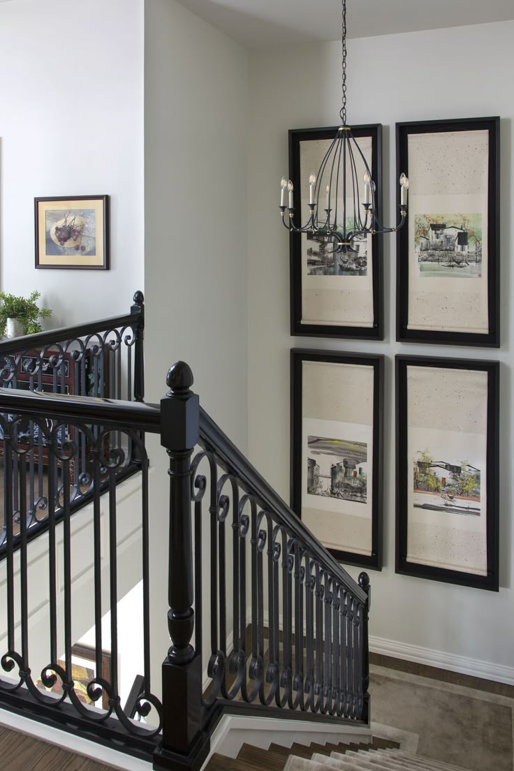 a staircase with pictures on the wall and chandelier hanging from it's handrail