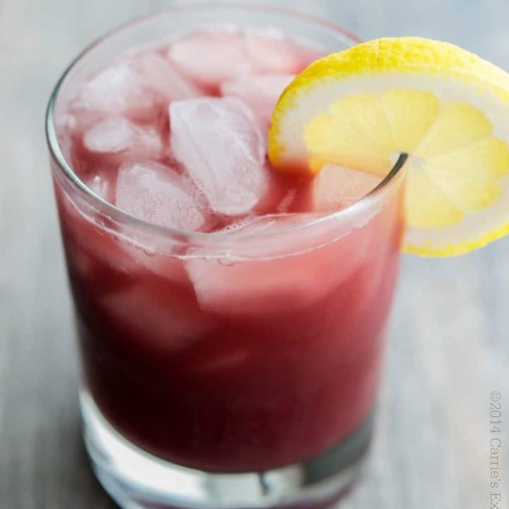 a close up of a drink with ice and a lemon slice on the rim,