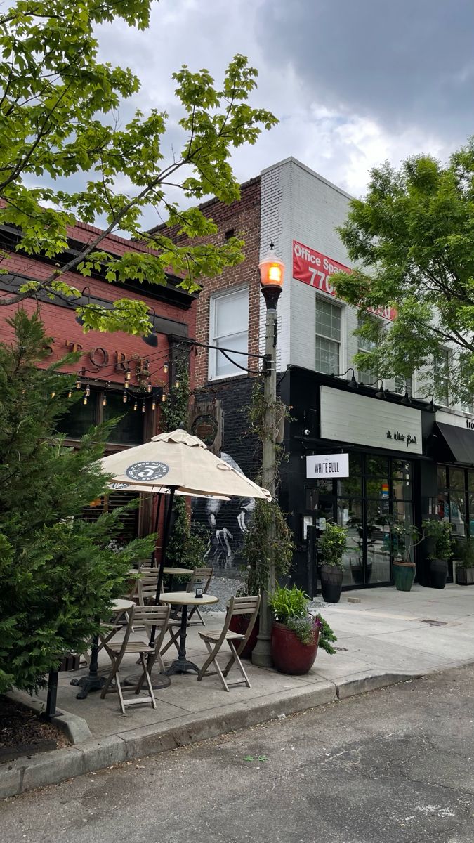 an outdoor cafe with tables and umbrellas on the sidewalk in front of a building